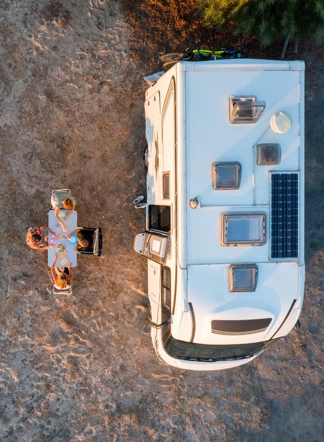 Aerial view of an RV equipped with solar panels and a family dining outdoors during a Canadian camping trip